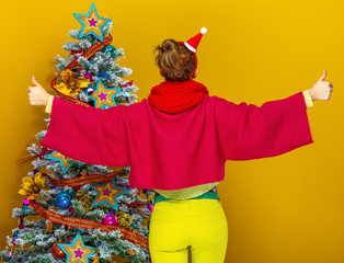 Wall Mural - stylish woman near Christmas tree showing thumbs up