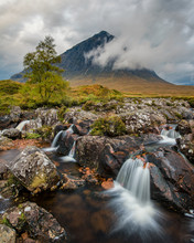 Picturesque Waterfall By The River With Buacheille Etive Mor In The Background Surrounded With Morning Mist.