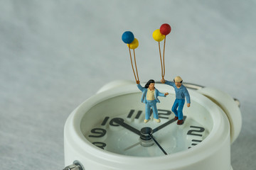 Wall Mural - miniature happy family holding balloons standing on white alarm clock as happy people on time deadline concept