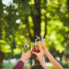 Group of people do cheers with detox juice cocktails on green nature background witn free space. Diet on the go, well being and weight loss, superfoods, health, vegetarian food concept