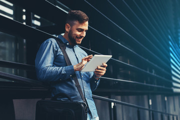 Handsome young man using digital tablet leaning against the wall