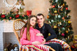 © Nestyda - Beautiful pregnant couple in love on the background of a Christmas tree, having a rest on Christmas holidays before the new year. Big pregnant belly