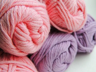 Pink and lilac cotton yarn balls for knitting and crocheting on white background.