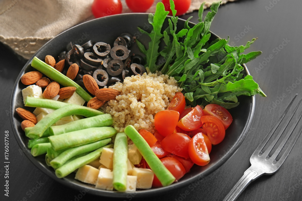 Plate with quinoa and vegetables on black background
