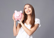 © Africa Studio - Beautiful young woman with piggy bank on grey background