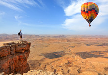Beautiful Landscape Of Stony Desert And Rocks And Colorful Hot Air Balloon Flight In The Blue Sky. Traveler Is On The Mountain Top Viewpoint