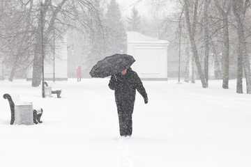 bad weather in winter: a heavy snowfall and blizzard in city. male pedestrian hiding from the snow u