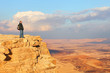 Traveler (hiker man) on a mountain edge top. Colored sand stone desert under beautiful sky before sunset. Unique geological erosion land form. National park Makhtesh Ramon (Crater). Negev, Israel