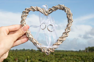 form of a heart with wedding rings in blue sky with vineyards background