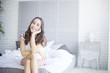 © My Ocean studio - Beautiful young brunette woman sitting at the end of the white bed.