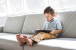 © Louis-Paul Photo - Little boy with digital tablet sitting on sofa, on home interior background