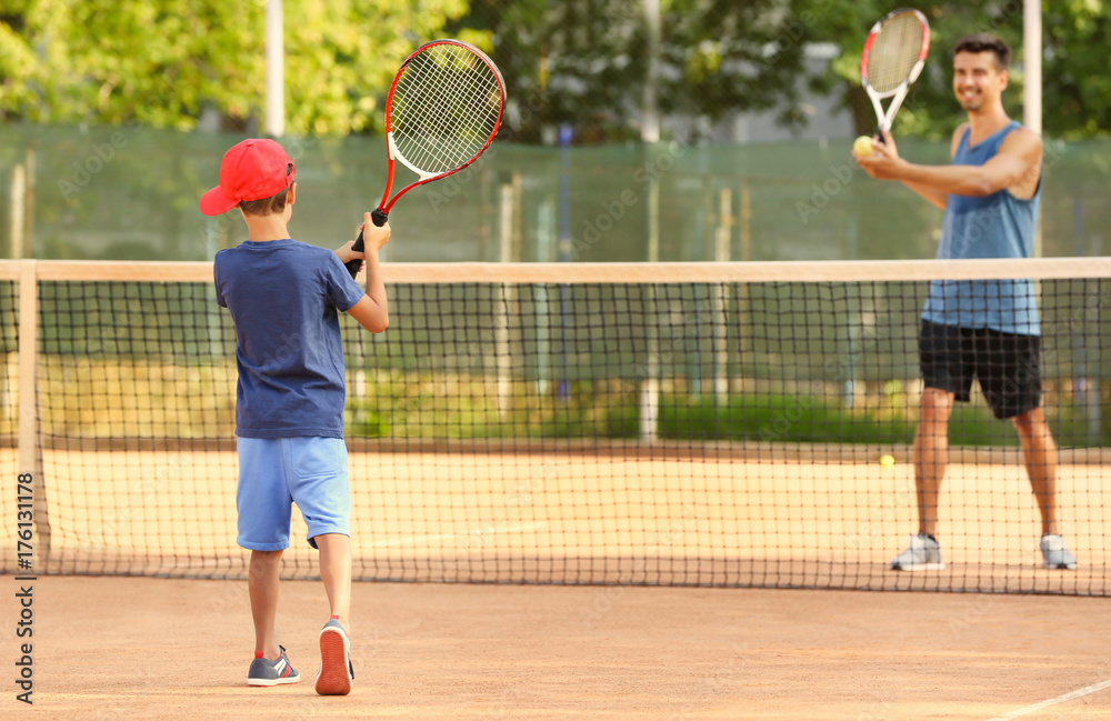 Young trainer with little boy playing tennis on court