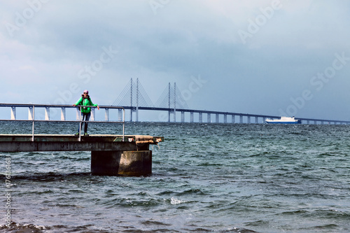 Fotografie, Tablou Happy woman tourist posing on the Oresund Bridge background.