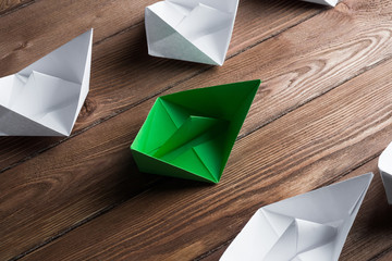 Business leadership concept with white and color paper boats on wooden table