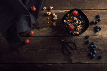 Cereal bowl with fresh fruits on dark old wood table top. Healthy breakfast ingredients with granola and berries. Top view.