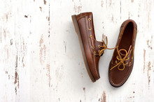Brown leather men's top sider shoes or boat shoes on a white wooden board. Fashion advertising shoes photos.