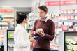 © Kzenon - Experienced female pharmacist checking the indications and contraindications of a new medicine next to a young male customer in a modern pharmacy