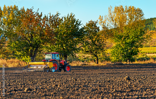 Fényképezés Farmer with tractor seeding - sowing crops at agricultural fields in autumn