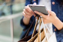 Close Up Of Woman Using Cellphone And Holding Shopping Bags