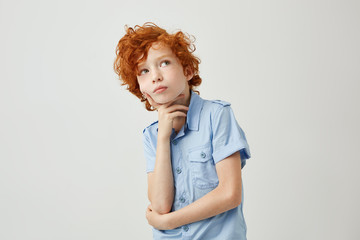 Wall Mural - Funny ginger little boy with wavy hair and freckles dreamy looking aside trying to remember if he did homework for school