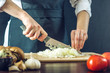 © Artem - The chef in black apron cuts an onion with a knife. Concept of eco-friendly products for cooking