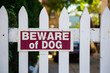 Beware of dog sign on white picket fence
