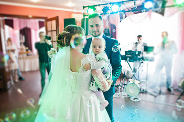 Wall Mural - Fantastic young beautiful wedding couple dancing in the restaurant with their little baby.