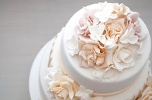 Three-tiered White Wedding Cake Decorated With Flowers From Mastic On A White Wooden Table. Picture For A Menu Or A Confectionery Catalog. Top View.