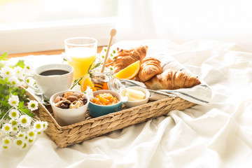 Wicker tray with continental breakfast on white bed sheets