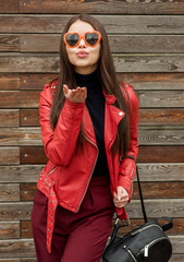 Wall Mural - Beautiful smiling brunette woman in sunglasses over wooden background. Sends Air kiss. Street fashion. Outdoors.