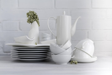 Wall Mural - White porcelain dishware stacked against white brick background. Concept of restaurant, food, cooking and service. Selective focus. Copy space. 