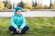 © olgasparrow - Beautiful teenage girl dressed in a warm jacket and hat sitting on the grass in the autumn.