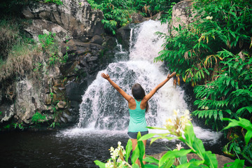 Hawaii travel nature waterfall woman hiker at Canyon Trail Waipoo Falls in Waimea, Kauai island, USA. Freedom happy girl with open arms meditating yoga in rainforest.