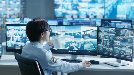 Leinwandbilder - In the Security Control Room Officer Monitors Multiple Screens for Suspicious Activities, He Drinks from a Mug. He's Surrounded by Monitors and Guards Port of National Importance. 