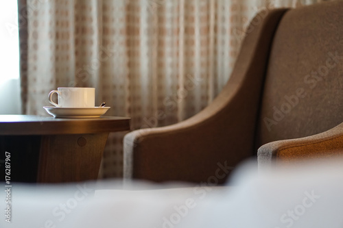 Plakat biały kubek kawy na stole przez kanapę w pokoju hotelowym