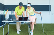 Cheerful young woman analyzing and watching on laptop her video recorded strike during a contemporary golf class with an experienced instructor