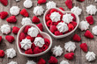 Raspberries and white meringues in two heart shaped ceramic jars overhead closeup on old rustic wooden table in studio