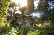 A close-up photo of a smoking paintball gun barrel being shot by a person laying in the forest in camouflage clothes