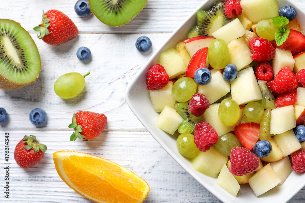 Bowl with yummy fruit salad on wooden table
