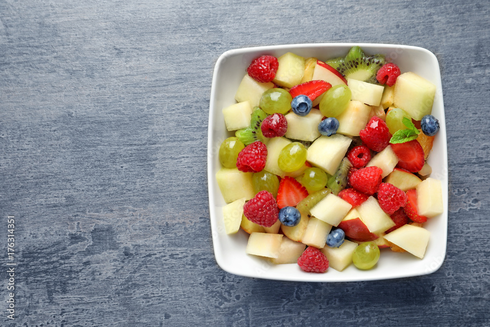 Bowl with yummy fruit salad on grunge table