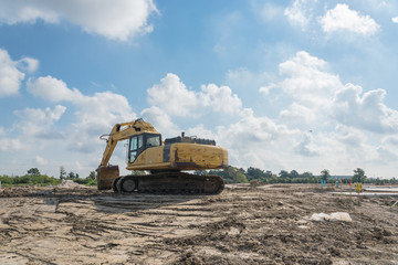 Excavator with digger standing for earthmoving works at construction site with storm cloud blue sky in Houston, Texas, USA. Framework for the concrete foundation of new building. Machinery background