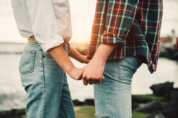 Happy couple in love holding hands at sunset time on the ocean wearing casual jeans outfit