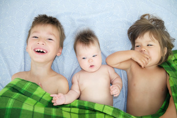 Canvas Print - Happy smiling children in family: brother and two little sisters. Boy, baby girl and little girl sibling kids lying on bed