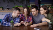 © kustvideo - A company of friends who sit in a restaurant and wait for their meals, look with joy and laugh at photos on the mobile phone that were made during the holiday