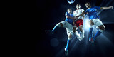 Fototapeta Sport - Soccer players performs an action play on a dark background. Soccer players fight for the ball. Players wears unbranded sport uniform.