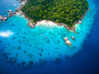 Top aerial view of isolated beautiful tropical island with white sand beach, blue clear water and granite stones. Also top view of speedboats above coral reef. Similan Islands, Thailand.