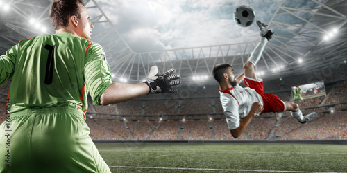 Zdjęcie XXL Piłkarz uderza piłkę do bramki na profesjonalnym stadionie. Bramkarz chroni bramę do piłki nożnej. Gracze mają na sobie niezarejestrowany mundur sportowy.