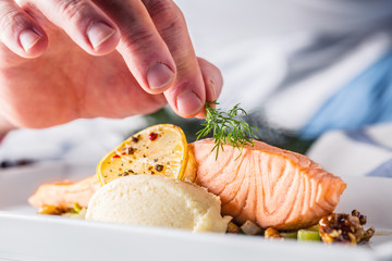 Chef in hotel or restaurant kitchen cooking, only hands. Prepared salmon steak with dill decoration