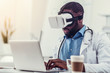 Serious medical worker in VR goggles working on laptop
