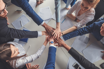 Unity concept. Close-up of people holding hands together while sitting around the desk